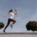 Athletic woman running on an outdoor road, demonstrating fitness and determination under a blue sky.