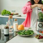 Woman in pink sleeve blending fresh fruits and veggies for a healthy smoothie.